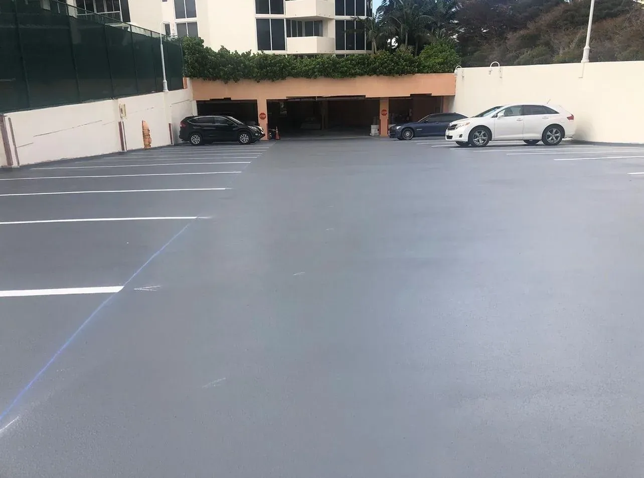Open-air condominium parking deck coated in grey slip-resistant traffic membrane with fresh white stall lines, building and hedges behind